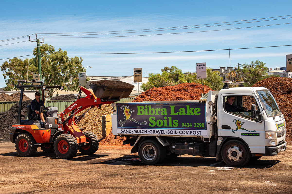 Tractor pouring soil into white delivery truck at Bibra Lake Soils